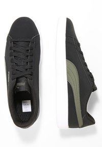 Zapatillas deportivas negras con un upper texturizado, banda de acento verde, mediasuela blanca y cordones negros. Diseño plano con punta redondeada.
