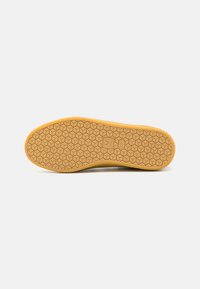 Rubber shoe sole with a honeycomb pattern in light brown. Features a logo and a flat edge at the front. Smooth, durable texture.