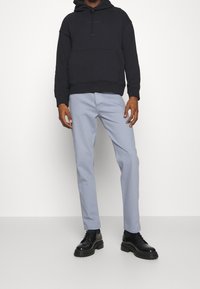 Černá mikina s kapucí a přední kapsou, světle modré chinos kalhoty a černé šněrovací boty s masivní podrážkou, umístěné na jednoduchém bílém pozadí.