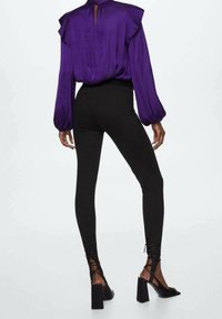 Lila Bluse mit gepufften Ärmeln, kombiniert mit schwarzen, hochtaillierten Leggings und schwarzen Sandalen mit Blockabsatz und Knöchelriemen.