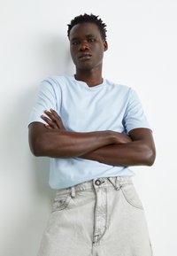 Light blue cotton crew-neck t-shirt and light gray denim shorts. The shirt features short sleeves and a subtle logo detail.