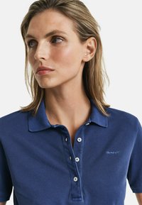 Marineblauw polo-shirt met een kraag, een drieknoopsluiting en geborduurd logo. Gemaakt van textuurstof met korte mouwen.