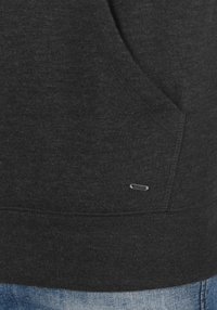 Dark gray hoodie with a soft texture, featuring a front pocket and a small metallic logo accent near the hem. Paired with blue jeans.