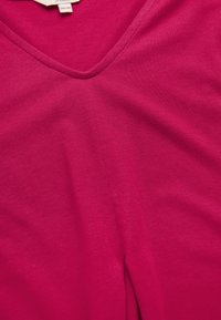 Fuksia v-kauluksellinen paita, joka on valmistettu pehmeästä, kevyestä kankaasta, jossa on sileä pinta. Vähäisiä saumoja, ei kuvioita tai koristeita. Tagi näkyvissä kauluksessa.