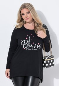 Schwarzes Langarmoberteil mit einem Grafikdesign des Eiffelturms, auf dem "Paris" sowie Herzen in Weiß und Rosa abgebildet sind, kombiniert mit einer Handtasche im Punktedesign.