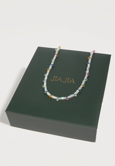 Collier délicat à perles multicolores et translucides présenté sur une boîte vert foncé avec lettrage doré.