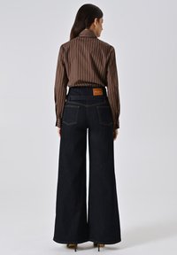 Wijdvallende donkere spijkerbroeken met een hoge taille, aangevuld met een bruin gestreepte lange mouw shirt. Bruin leren label aan de achterkant.