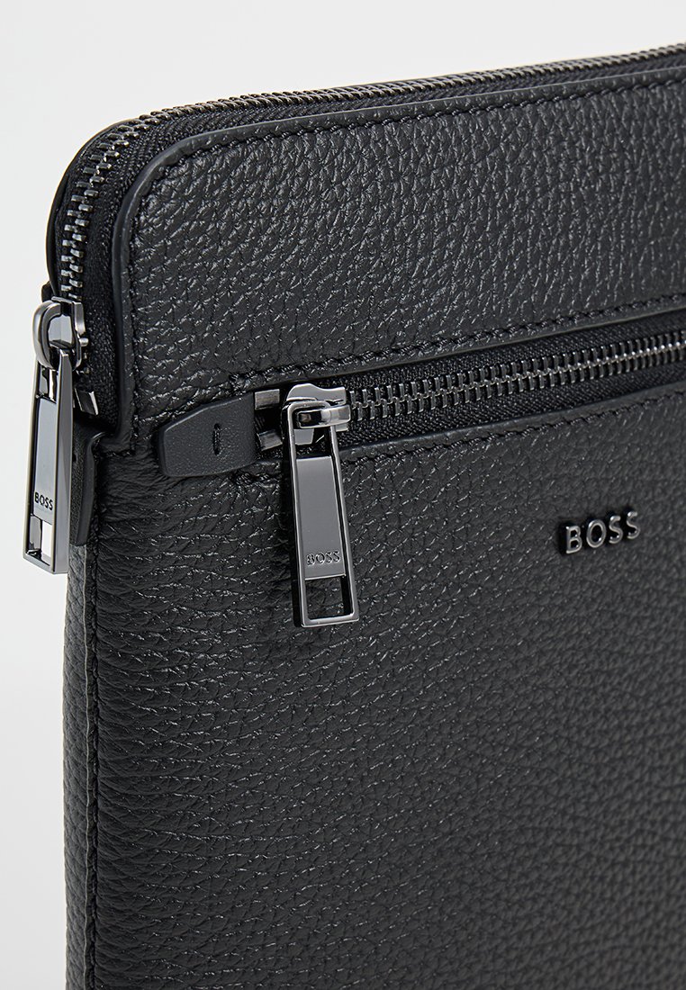 Pochette en cuir noir avec finition texturée, dotée d'une grande fermeture éclair et d'accents en métal, logo embossé et bords lisses.