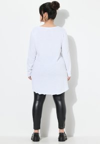 Biała tunika z długim rękawem i okrągłym dołem, w połączeniu z czarnymi skórzanymi legginsami. Modelka nosi masywne czarne buty. Minimalistyczny design, bez wzorów.