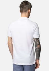 Biała koszulka polo z krótkim rękawem, wykonana z przewiewnego materiału. Posiada subtelne logo przy kołnierzyku oraz prosty dół.