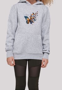 Felpa grigia con grafica di una farfalla in blu e arancione, dotata di tasca frontale e polsini a coste. Indossata con leggings neri con pannelli trasparenti.
