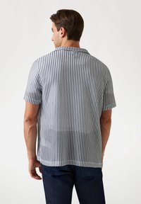 Camisa de manga corta con un patrón de jaquard en blanco y negro, cuello y corte recto, hecha de un tejido ligero y tejido.