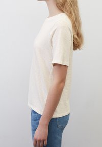 Tričko s krátkým rukávem a kulatým výstřihem v bledě béžové barvě, vyrobené z měkké látky a s volným střihem, doplněné modrými džíny.