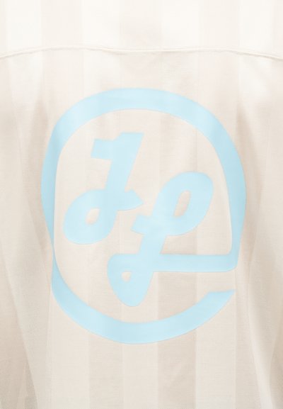 Initiales stylisées « JP » en bleu clair, enfermées dans un cercle, imprimées sur un tissu texturé de couleur blanc cassé.