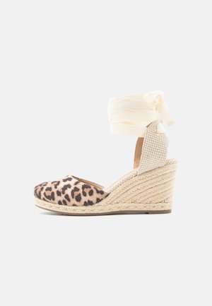 Espadrille à plateforme avec bout en imprimé léopard, talon en jute tressé et lien crème à nouer autour de la cheville sur fond blanc.