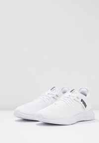 Bílé atletické boty s síťovinovým svrškem, plochými tkaničkami a polstrovanou podrážkou. Doplňují je černé logo na boku a strukturovaný materiál.