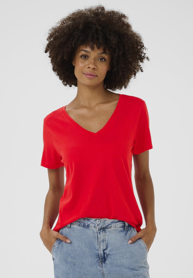 Piros, rövid ujjú póló V-nyakkal. Simogatós anyagból készült, laza szabással, világoskék farmernadrággal párosítva.