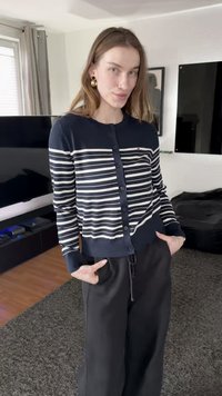 Καρντιγκάν με ναυτικό μπλε και άσπρες ρίγες, στενή γραμμή, μακριά μανίκια, σε συνδυασμό με μαύρο παντελόνι. Εσωτερικός χώρος με σκούρο καναπέ.