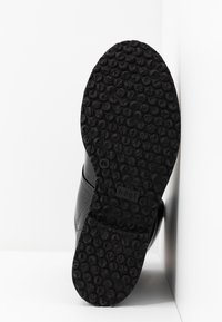 Suela de goma negra con una superficie texturizada que presenta patrones redondos. Parte superior de cuero liso con un diseño curvado y una marca mínima visible.