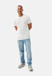 Vit crew neck t-shirt med avslappnad passform, kombinerad med ljusblå jeans och grönaktiga sneakers med vit sula. Minimalistisk design, inga mönster.