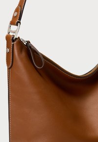 Cauri brūnas ādas plecu soma ar gludu tekstūru, izliekta augšējā mala un kontrastējošs šuvums. Ietver sudraba toņa aparatūras sprādzi un siksnu.