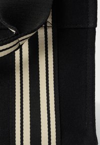 Borsa in tessuto nero con superficie texturizzata e un accento a strisce bianche. La fodera interna è leggermente visibile, migliorando il contrasto visivo.