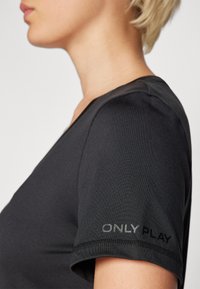 Must tume mustegad, lühikeste varrukatega, V-kaelusega ja tekstureeritud kangast. "ONLY PLAY" logo on hallina varrukal.