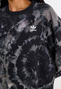 Black and grey tie-dye sweatshirt featuring a round neckline, dropped shoulders, and a small white adidas logo on the chest.