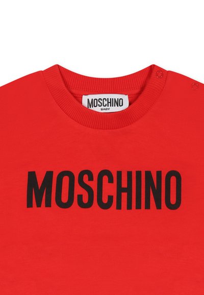 T-shirt in cotone rosso con colletto rotondo, bottoni a pressione sulla spalla e un audace logo nero "MOSCHINO" sul davanti.