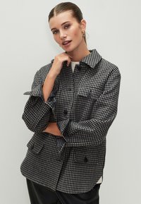 Giacca a quadri in bianco e nero, con collo, tasche anteriori e chiusura con bottoni; il tessuto presenta una texture con motivo pied de poule.