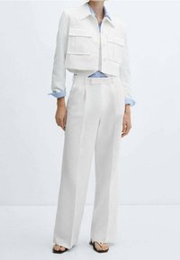 Valkoinen lyhyt takki, jossa kaksi etutaskua, yhdistetty korkeavyötäröisiin, leveälahkeisiin valkoisiin housuihin. Vaaleansininen kauluksellinen paita alla.