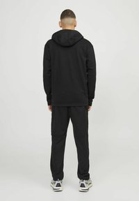 Black cotton hoodie with a hood, long sleeves, and relaxed fit, paired with matching joggers. Notable details include ribbed cuffs and hem.