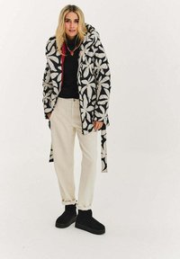 Prošívaná bunda s černobílým květinovým vzorem, červenou podšívkou, nošená přes černý top. Kombinováno s krémovými kalhotami a černými kotníkovými botami.