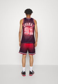Ensemble de maillot de basket et de shorts, noir avec dégradé rouge et rayures. Présente "RODMAN" et "91" en blanc gras. Stylisé avec des baskets noires.