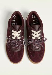 Bordeaux sportsko i mikro- og lædermaterialer, med cremefarvede snørebånd, flerfarvede mønstrede snørebånd og en gummisål.