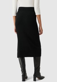 Svart stickad midi kjol med ribbat midjeband och struktur, med en figurnära design och slits i fållen för enkel rörelse.