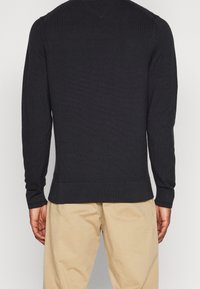 Schwarzer gerippter Strickpullover mit langen Ärmeln, V-Ausschnitt und tailliertem Schnitt, der ein strukturiertes Muster und einen geraden Saum aufweist.