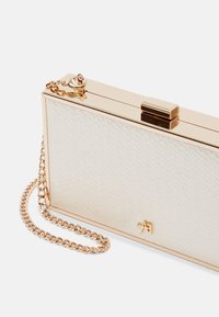 Pochette rectangulaire beige avec surface texturée, cadre doré, fermeture à fermoir, petit logo doré et chaîne amovible dorée sur fond blanc.