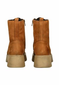 Botas de tobillo de cuero marrón con una textura suave, que presentan un cierre lateral con cremallera y un tacón grueso en tono beige. Diseño sencillo con detalles de costura visibles.