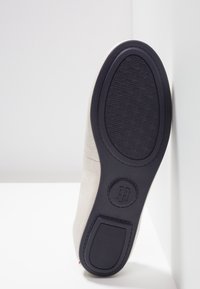 Jasnoszare skórzane buty z teksturowaną czarną gumową podeszwą. Posiadają szczegół w postaci okrągłego logo oraz gładki, bezszwowy design.