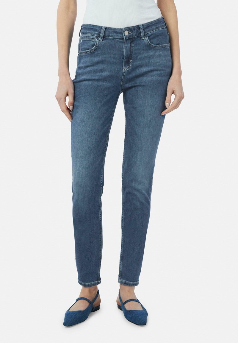 Skinny jeans in een middentint denim, met een klassieke vijfzakkenontwerp, ritsvlieg met knoop en subtiele vervaging. Gecombineerd met blauwe ballerina's.