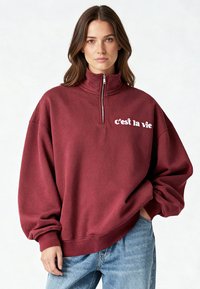 Sweat-shirt bordeaux zippé avec col montant, coupe décontractée et texte blanc "c'est la vie" sur le côté gauche de la poitrine. Tissu en mélange de coton, poignets côtelés.