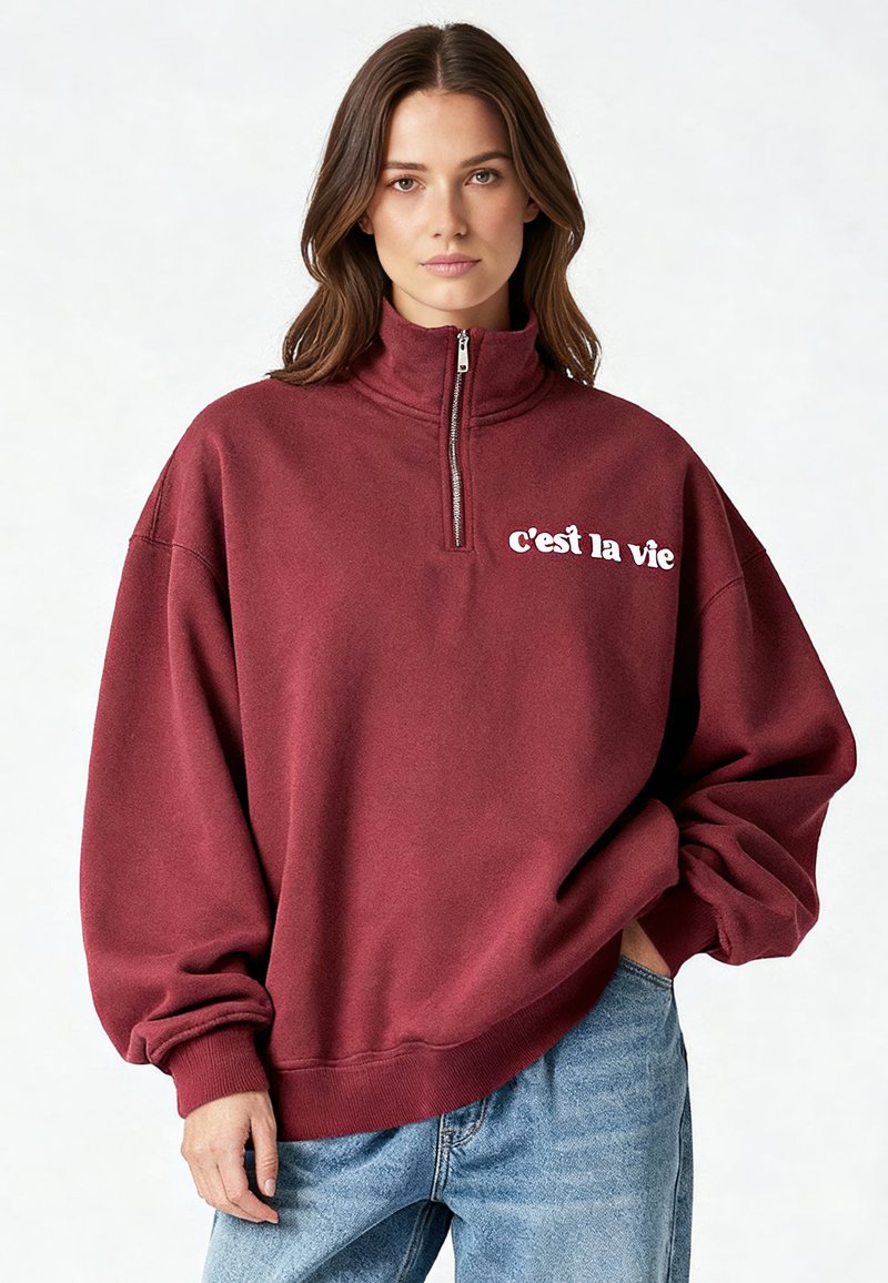 Sweat-shirt bordeaux zippé avec col montant, coupe décontractée et texte blanc "c'est la vie" sur le côté gauche de la poitrine. Tissu en mélange de coton, poignets côtelés.