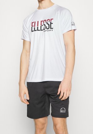 Camiseta deportiva blanca de manga corta con el logo "ELLESSE SPORT" en negro y rojo, combinada con pantalones cortos negros con un pequeño logo blanco.