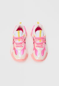 Sportssko med et skinnende hvitt, rosa og iriserende design. Har rosa snøringer, en gul løkke på hælen og teksturerte såler.