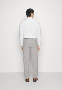 Bela srajca s knoflji, svetlo siva hlače in rjavi čevlji. Srajca ima standardni ovratnik; hlače so krojene in imajo gube.