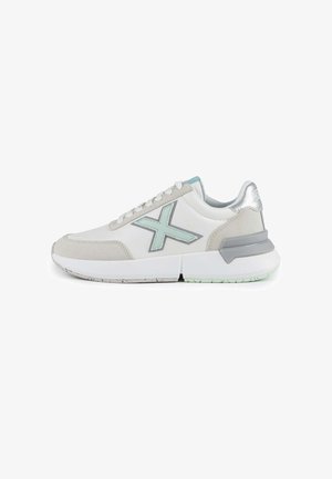 Zapatillas deportivas blancas con una puntera de ante gris, acentos en azul claro, un contrafuerte plateado y una suela blanca gruesa.