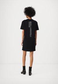 Svart t-shirt klänning med korta ärmar, med en vertikal vit logotryck på baksidan. Bärs med svarta klackboots till anklarna.