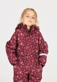 Bordeaux sneeuwpak met bloemenpatroon, gevoerde ontwerp, rits aan de voorkant en elastische manchetten. Heeft reflecterende accenten op de mouwen en zakken.
