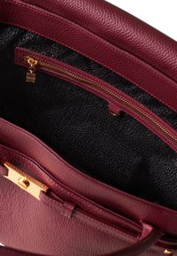 Borsa in pelle borgogna con texture a ciottoli. Caratterizzata da una tasca con zip dorata e foderata con un motivo nero. L'interno ha una forma elegante e ben definita.